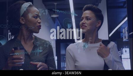 Walking two women talking in office hall, holding coffee, in business attire, showing data overlays Stock Photo