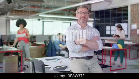 Sitting senior team lead wearing checkered shirt on table at design studio, with plans and helmets Stock Photo