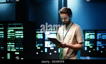 Repairman doing annual system servicing, imputing data on tablet of required upkeeping in server racks housing advanced data storage infrastructure supporting critical IT workloads Stock Photo