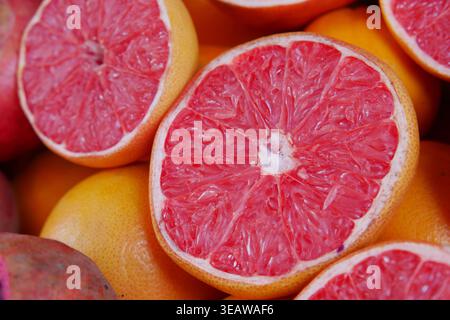 Fresh grapefruit cut in half among whole fruits on display Stock Photo