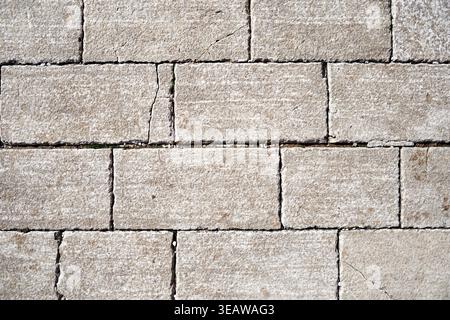 Weathered light gray stone wall texture with rectangular blocks and natural cracks. Ideal for architectural backgrounds or rustic design concepts Stock Photo