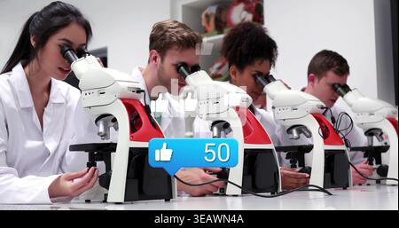 Examining students using white-red compound microscopes in lab in lab coats and blue likes overlay Stock Photo