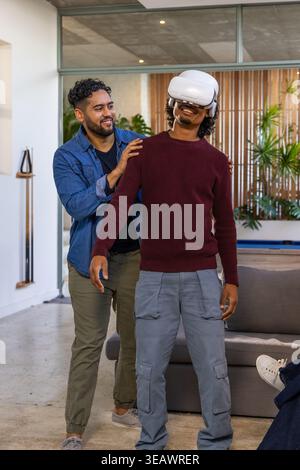 Male friends steadying man wearing white VR headset while standing in loft lounge with pool cues Stock Photo