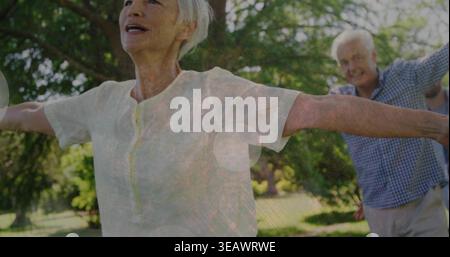 Stretching senior woman extending arms in park, wearing light blouse with man in checkered shirt Stock Photo
