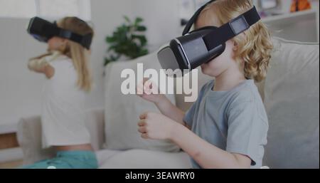 Playing girl in light blue t-shirt reaching with hands on couch at home, wearing VR headsets Stock Photo