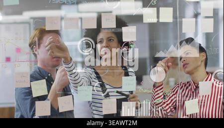 Pointing center woman holding marker, two colleagues in office attire pointing at glass with notes Stock Photo