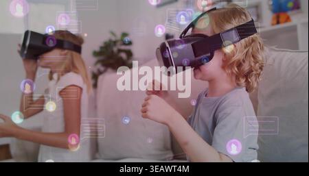 Playing two children wearing VR headsets in casual shirts on living room sofa, using floating UI Stock Photo
