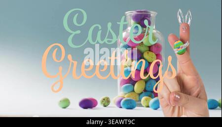 Displaying jar and two finger bunnies forming on table with speckled eggs, Easter Greetings text Stock Photo