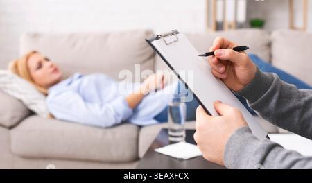 Psychologist listening to depressed patient and writing down notes Stock Photo
