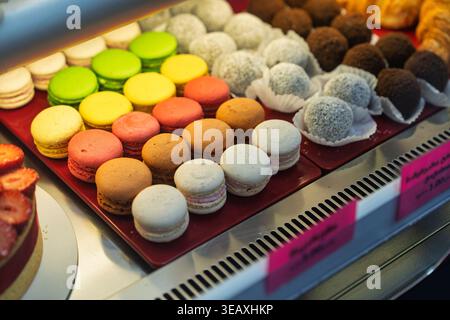 Assortment of vibrant macarons, chocolate truffles, and other sweet bakery items arranged appealingly in a refrigerated display case inside a confecti Stock Photo