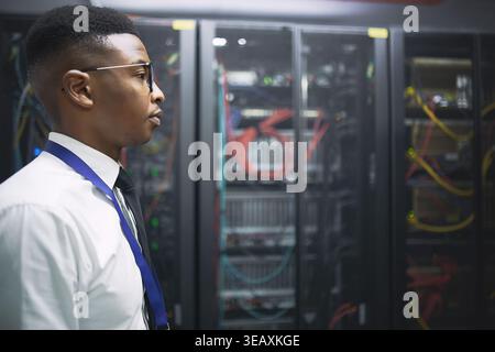 Serious, black man and technician walk in server room for inspection, cybersecurity and system alert. Person, monitor and data center for IT support Stock Photo