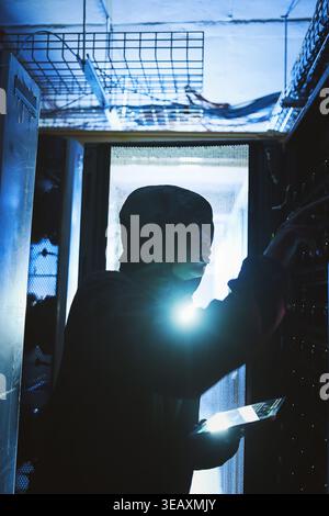 Person, hacker and tablet in data center at night for coding, cyber attack and ransomware. Suspicious, criminal and digital with code script for Stock Photo