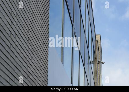 Borken, NRW, Germany, Modern building facade showcasing glass windows reflecting the sky, with a security camera mounted on the brick wall Stock Photo