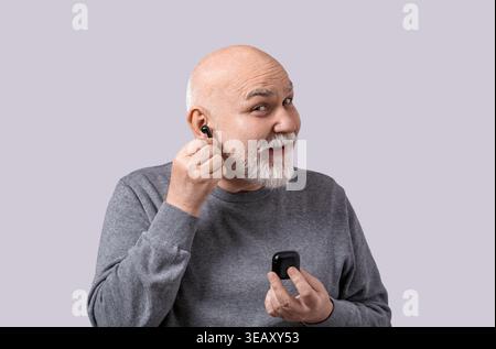 Mature man using wireless earphones. Old beard man wearing earbud listening to music in wireless headset. Male with earphones in the ear. Portrait of Stock Photo