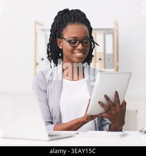 Woman With Glasses Enjoys Reading on Tablet While Working in Modern Office Space Stock Photo