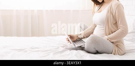 Woman Sitting on Bed Using Laptop While Expecting a Baby in Serene Indoor Space Stock Photo