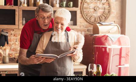 Senior Couple Enjoys Cooking Together While Looking at a Recipe Book in a Cozy Kitchen Stock Photo