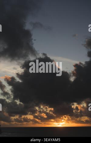 Airplane flying over dramatic sunset sky above ocean coast, Bali Stock Photo