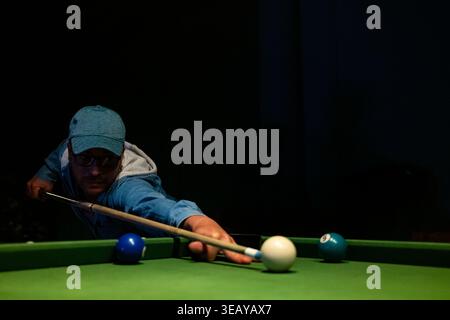Close-up of a billiard player taking a precise shot in a dark, atmospheric pool hall Stock Photo