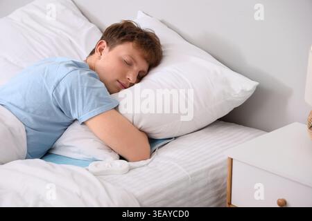 Young man sleeping on electric heating pad in bedroom Stock Photo