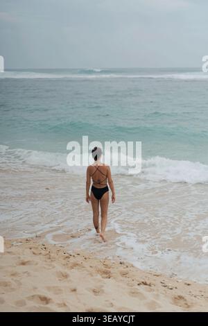 Woman in strappy bikini walking toward ocean waves, Uluwatu, Bali Stock Photo