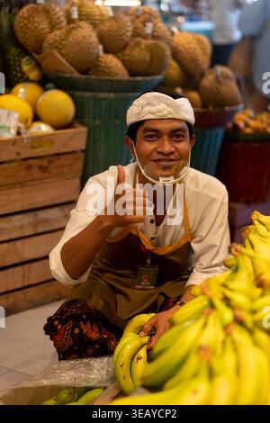Happy Balinese supermarket worker giving thumbs up near bananas, Bali Stock Photo