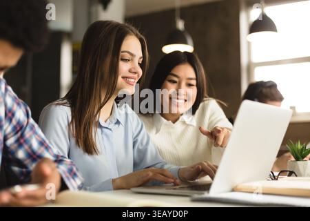 Two Friends Collaborate on a Laptop in a Modern Workspace While Smiling and Discussing Ideas Stock Photo