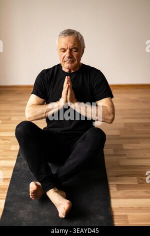 Senior man practicing mindfulness meditation on yoga mat Stock Photo