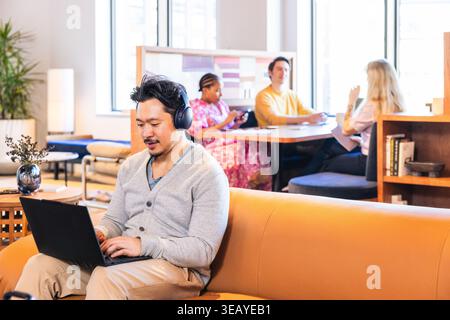 Asian Businessman Smiling and using headphones while on computer Stock Photo