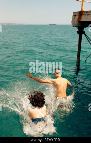 Two people leaping into turquoise sea on summer day Stock Photo