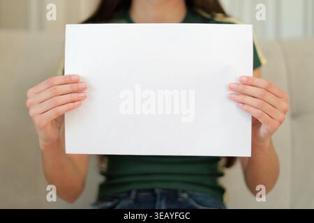 Person Holding Blank White Paper Sign. Close-up of a person holding a blank white sheet, ideal for message, announcement, advertising, or copy space Stock Photo