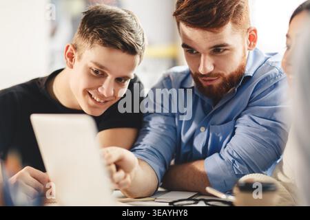 Two Young Men Collaborating on a Project While Seated at a Table With a Laptop in an Office Stock Photo