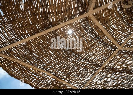 Braided straw providing shade in an outdoor setting, with bright sunlight filtering through the natural texture of the woven material, creating a summ Stock Photo