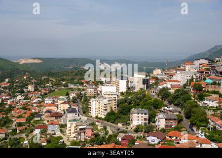 Panoramic view of Kruja city in Albania showing residential buildings and red roofs nestled against the green hills under a hazy blue sky Stock Photo