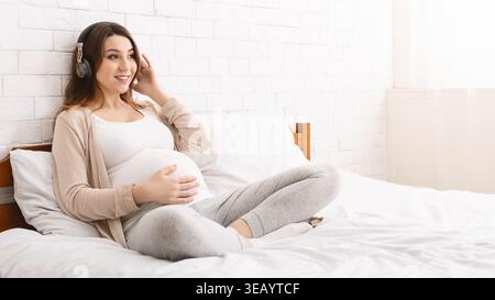 Expectant Mother Enjoying Music While Resting in a Bedroom Stock Photo