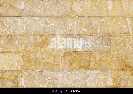 Stone wall made of marble or granite with yellow to brown wear marks and tiny joints between the stones Stock Photo