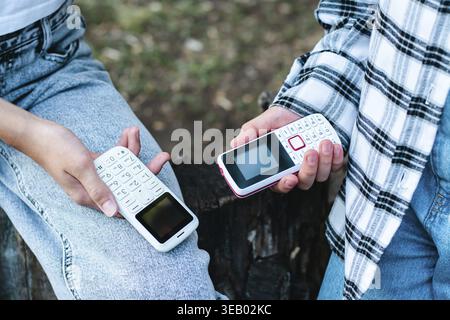 People in jeans hold push-button phones in their hands on their knees Stock Photo
