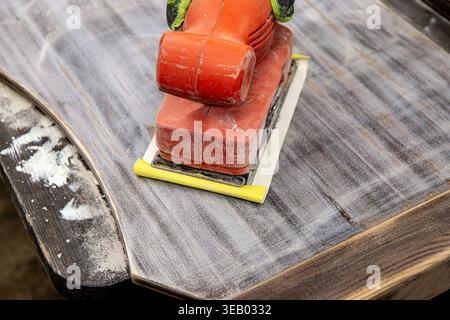 Close-up of sanding old varnish and paint off furniture with an orbital sander, so it can be reused and repainted. Close-up of a worker’s hand sanding Stock Photo
