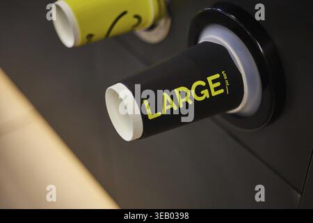 Coffee shop, store, cafe business. Colored paper cups, black glass with yellow inscription large in dispenser, big size for hot drinks, coffee, tea to Stock Photo