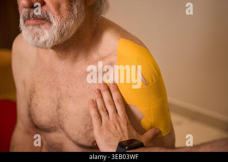 Elderly man receiving kinesiology tape treatment indoors Stock Photo