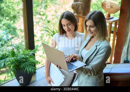 Two women collaborating in bright office with laptop and papers Stock Photo
