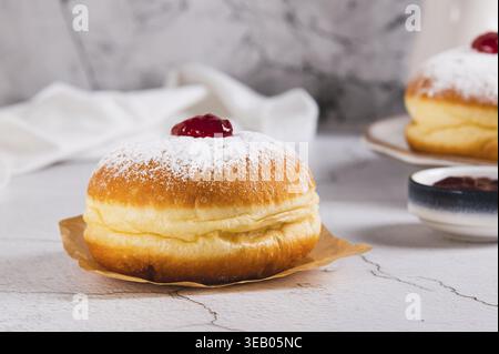 Delicious jam donuts in powdered sugar on parchment paper on the table Stock Photo