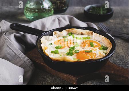 Homemade scrambled eggs in pita bread with herbs in a frying pan on the table Stock Photo