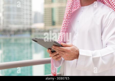 Arabic businessman stands near the water holding a tablet while in an urban environment. The city buildings surround him. Stock Photo