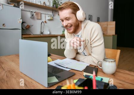 Stylish man wearing headphones laughs while participating in a virtual class at home. Stock Photo