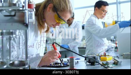 Soldering researcher in lab coat and yellow goggles working on PCB at bench, with soldering iron Stock Photo