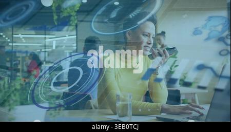 Typing woman in yellow turtleneck checking phone, working on laptop at open office with AR overlays Stock Photo
