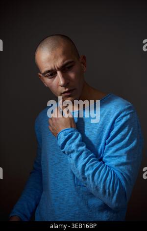 Studio portrait of a pensive man in a blue sweater. Concept of thinking, decision making, and mental focus. Neutral dark background. Stock Photo