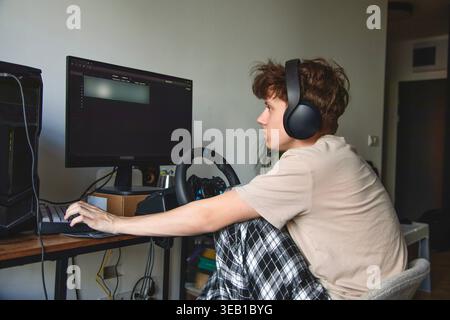 Young man playing racing video game with steering wheel and headset at home Stock Photo