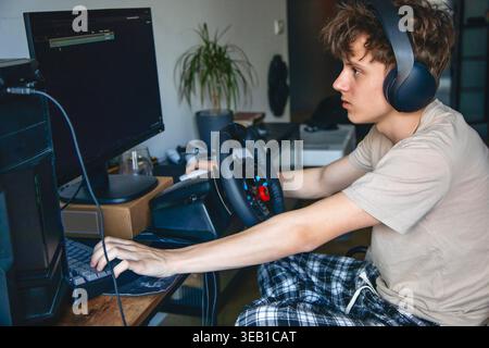 Young man playing racing video game with steering wheel and headset at home Stock Photo